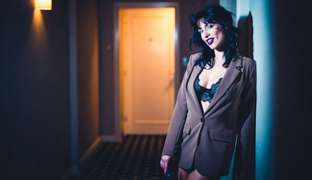 Donna elegante con blazer e top di pizzo in un corridoio d'hotel di notte - storia vera di tradimento con due amanti